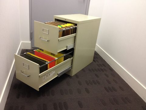 Filing cabinet with two open drawers full of hanging folders in an office corridor