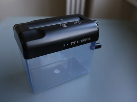 Kleiner Aktenvernichter mit durchsichtigem Auffangbehälter auf einem hellblauen Tisch