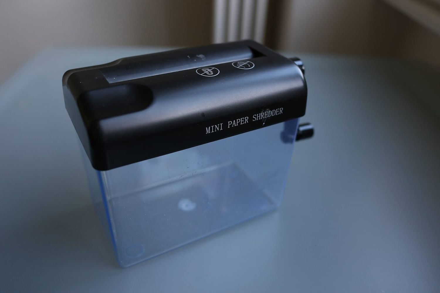 Small paper shredder with a transparent bin standing on a pale blue table
