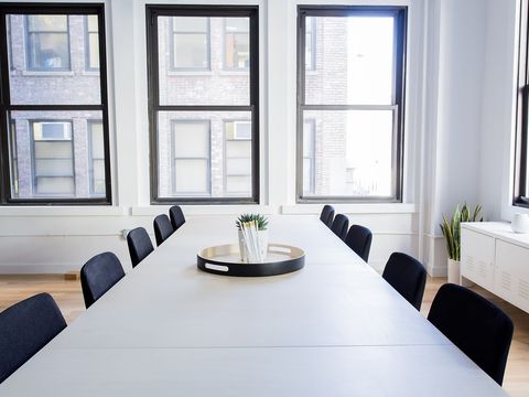 Leerer Besprechungsraum mit langem weißem Tisch, schwarzen Stühlen und hohen Fenstern