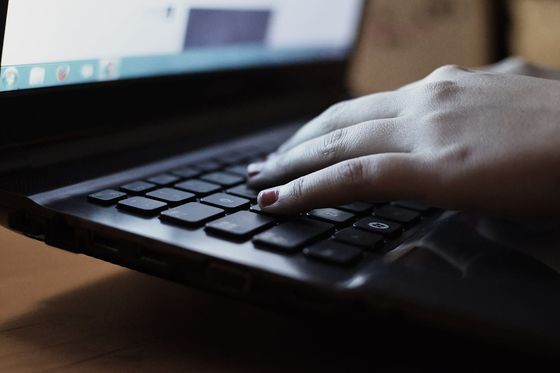 Eine Hand liegt auf der Tastatur eines schwarzen Notebooks, im Hintergrund leuchtet der Bildschirm