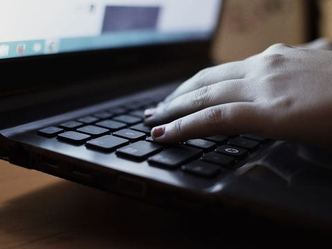 A hand resting on the keyboard of a black laptop with the screen glowing behind it