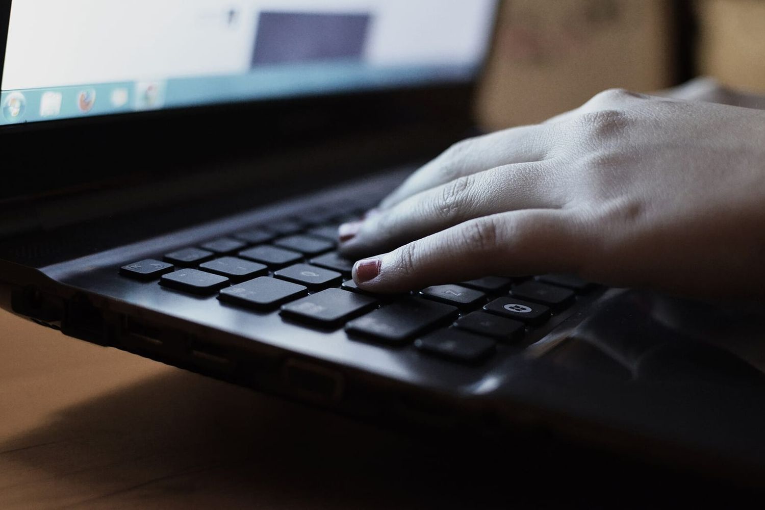 Eine Hand liegt auf der Tastatur eines schwarzen Notebooks, im Hintergrund leuchtet der Bildschirm