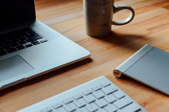 Aufgeräumter Arbeitsplatz mit Laptop, Tastatur, Trackpad und Keramiktasse auf hellem Holztisch