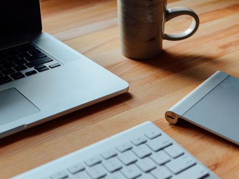 Tidy workstation with a laptop, keyboard, trackpad and ceramic mug on a light wooden desk
