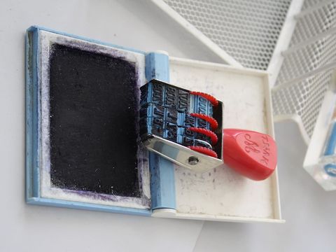 A date stamp with red adjustment wheels lying next to an open ink pad