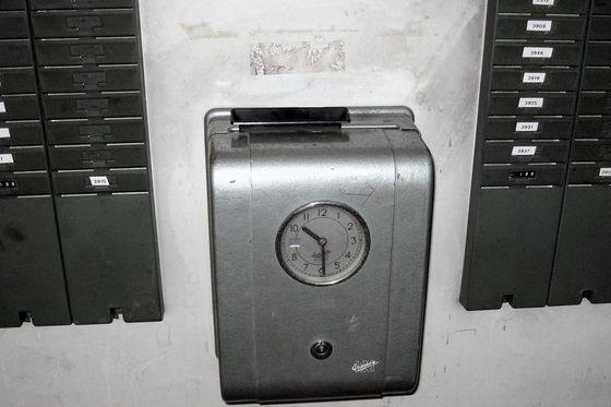 Old mechanical time clock on a wall between two racks of numbered time cards